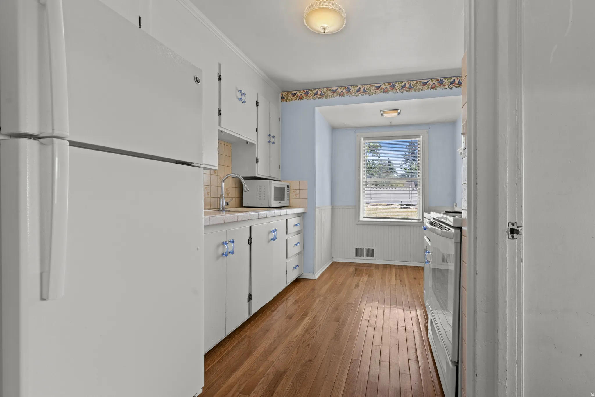 Kitchen with wood-finish flooring, white cabinetry, and a window overlooking the exterior