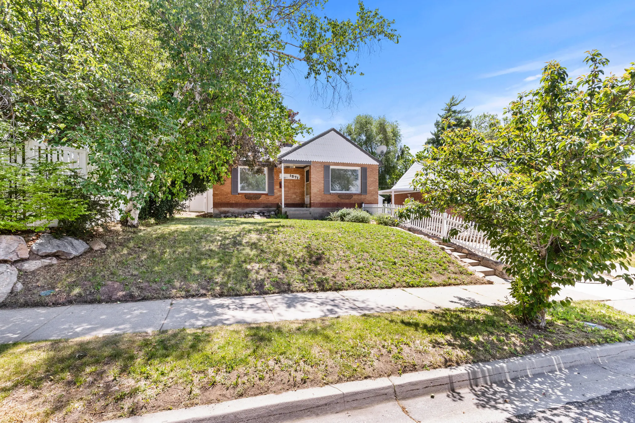 Brick residence with a white picket fence and mature landscaping