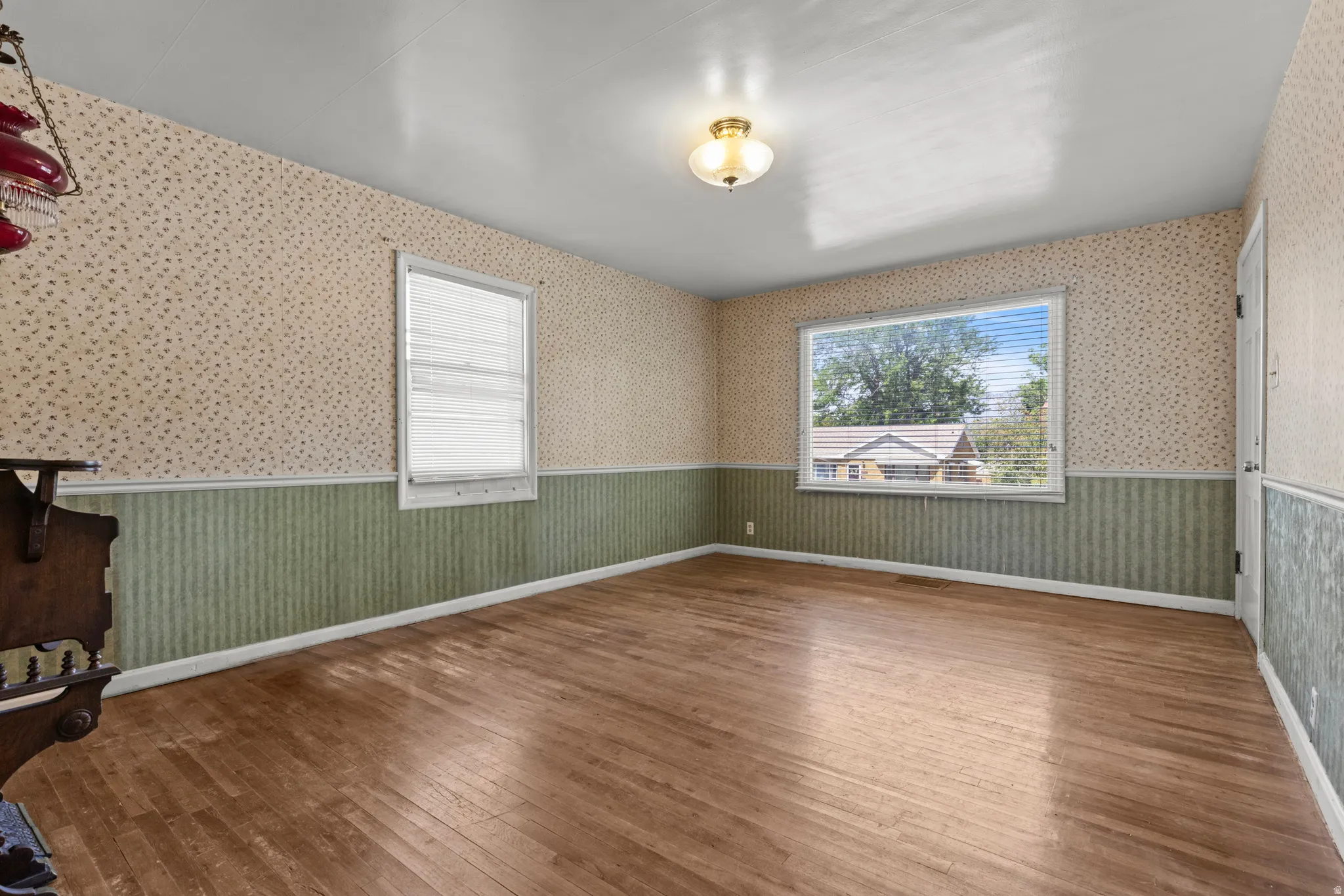 Room featuring hardwood flooring, two windows with blinds, a ceiling-mounted light fixture, and two-tone wall coverings