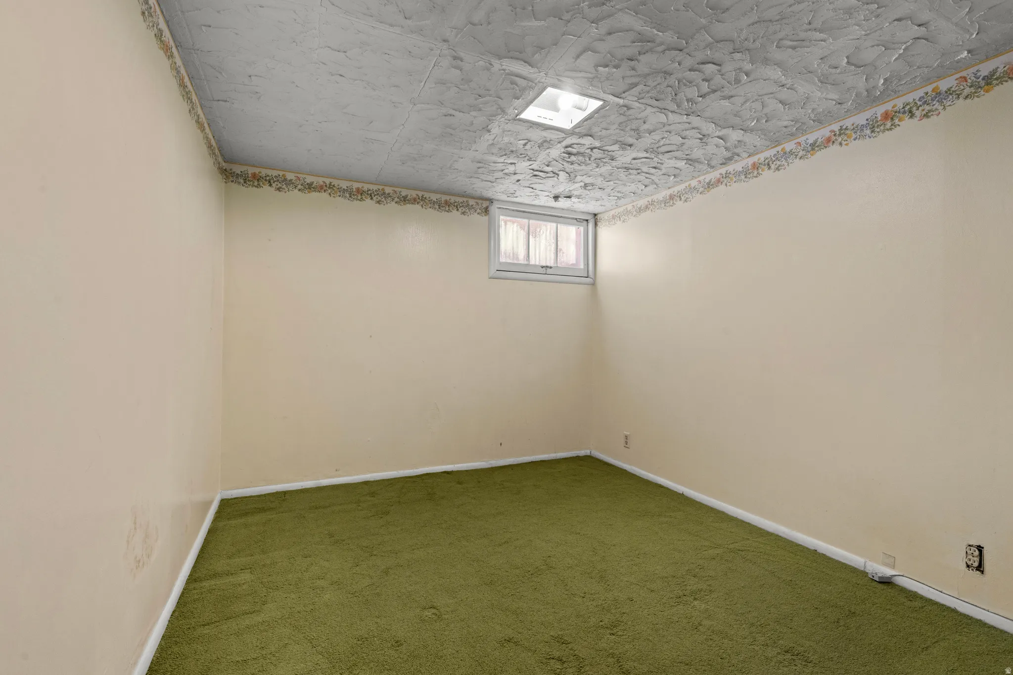 Room featuring textured ceiling, light-colored walls with decorative border, and green carpeting
