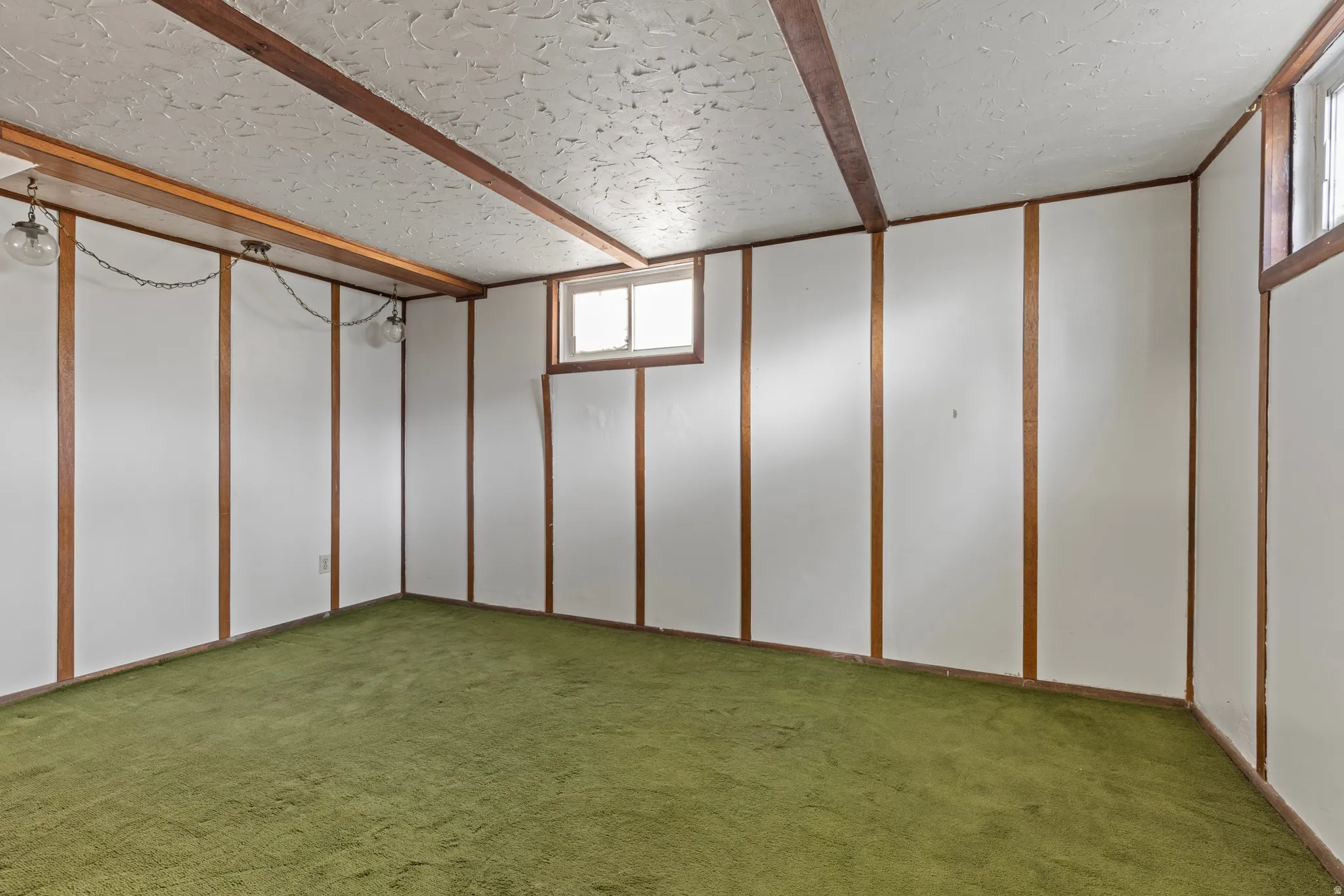 Room featuring green carpet, white wall panels with wood trim, and a textured ceiling with exposed wood beams