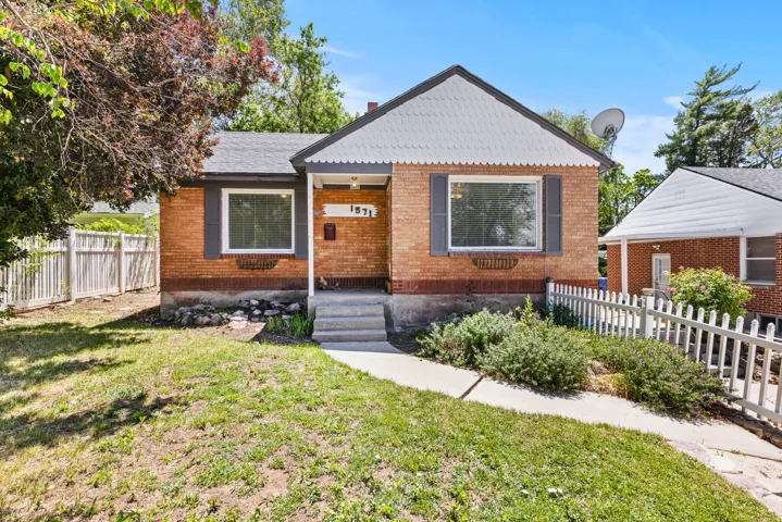 Brick-clad residence featuring a white picket fence, mature landscaping, and a concrete pathway leading to the entry