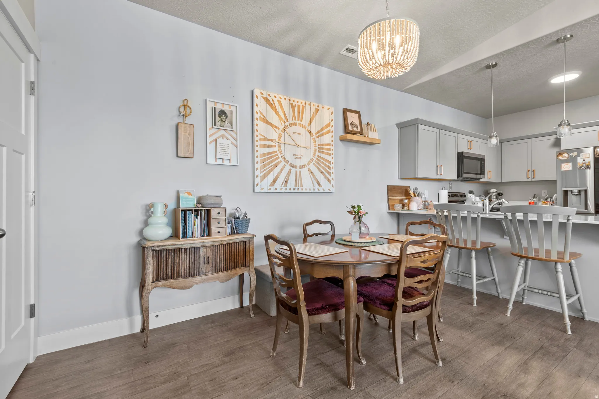 Open-concept dining area with wood-finish flooring, featuring a beaded chandelier and a kitchen beyond