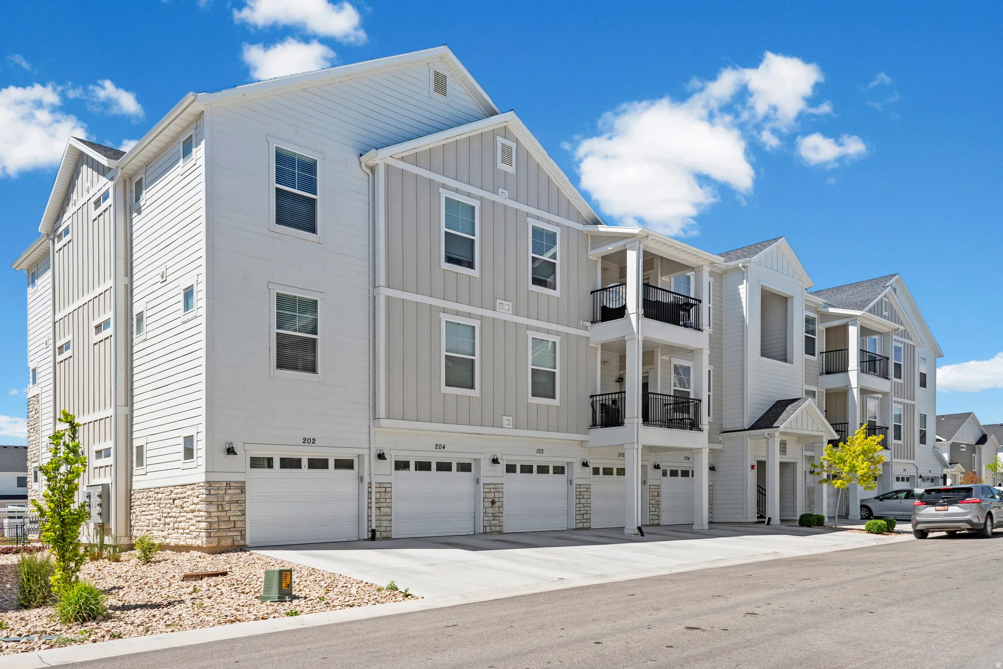 Modern multi-story building featuring white horizontal siding, light grey vertical siding, and stone veneer accents