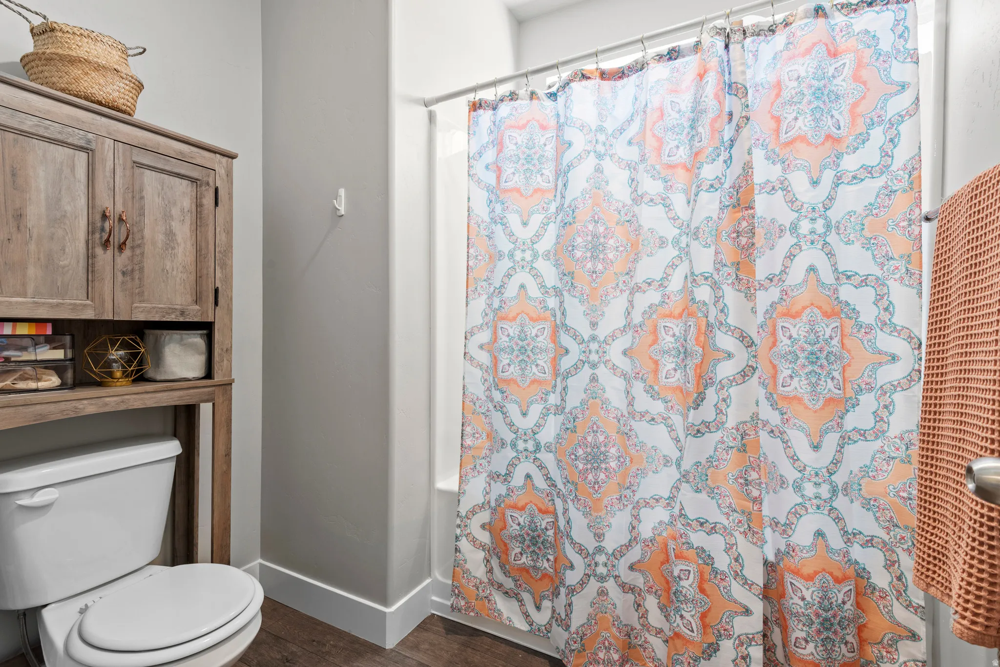 Bathroom featuring a white toilet, wood-finish storage cabinet, white baseboards, and wood-finish flooring