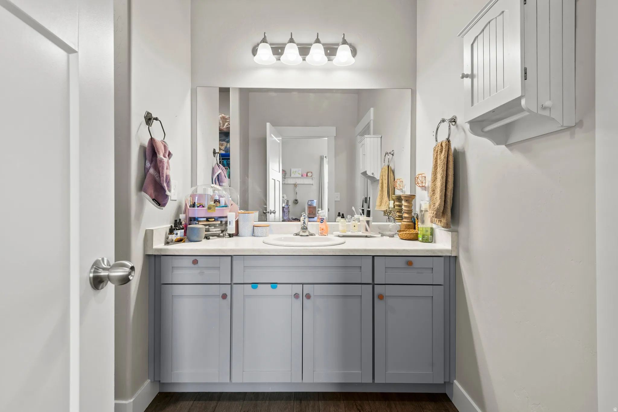 Bathroom vanity featuring light gray cabinetry with brass-finish hardware, a single basin sink, and a white countertop