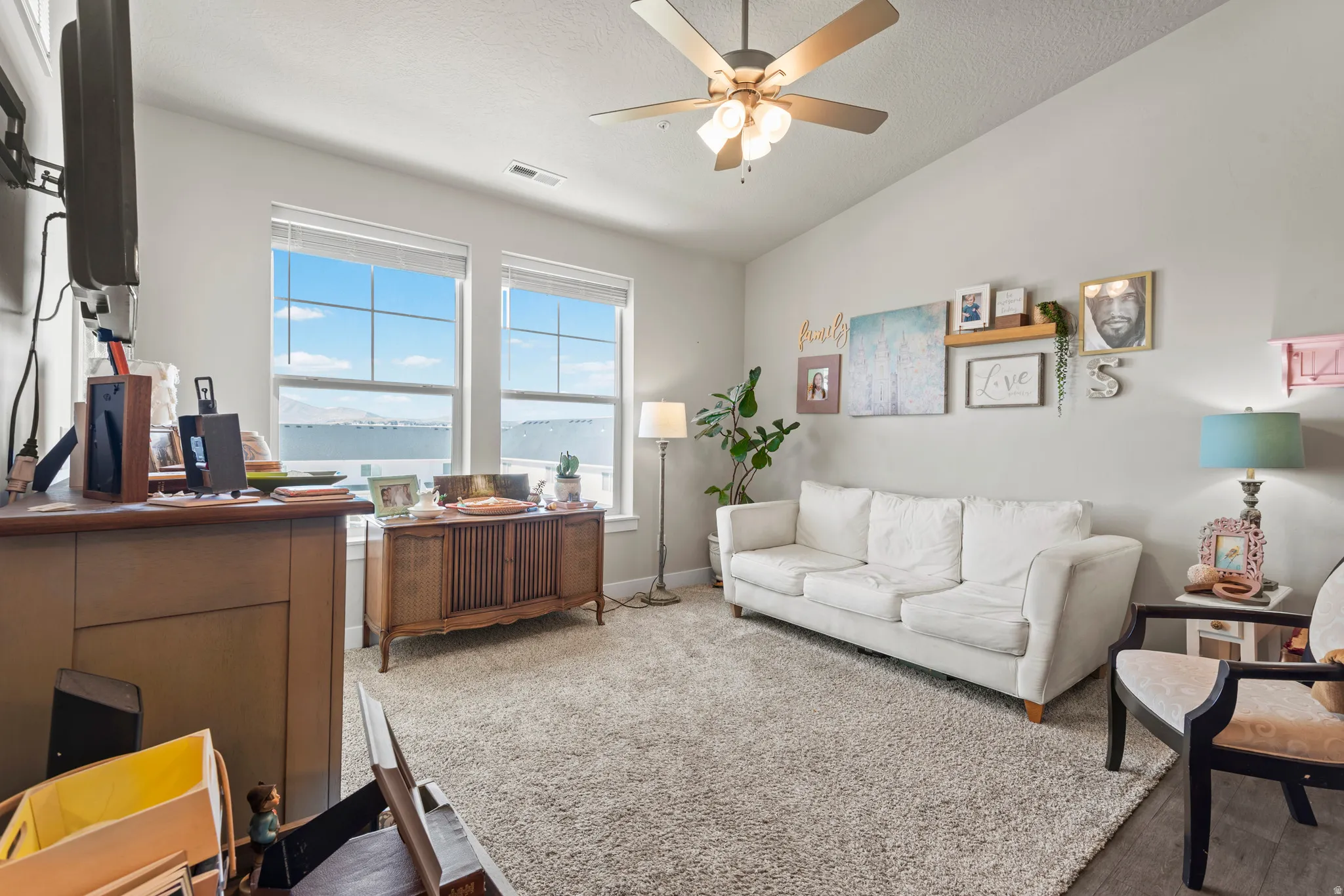 Bright living area featuring large windows with mountain scenery, a ceiling fan with integrated lighting, textured carpeting, and wood-finish flooring