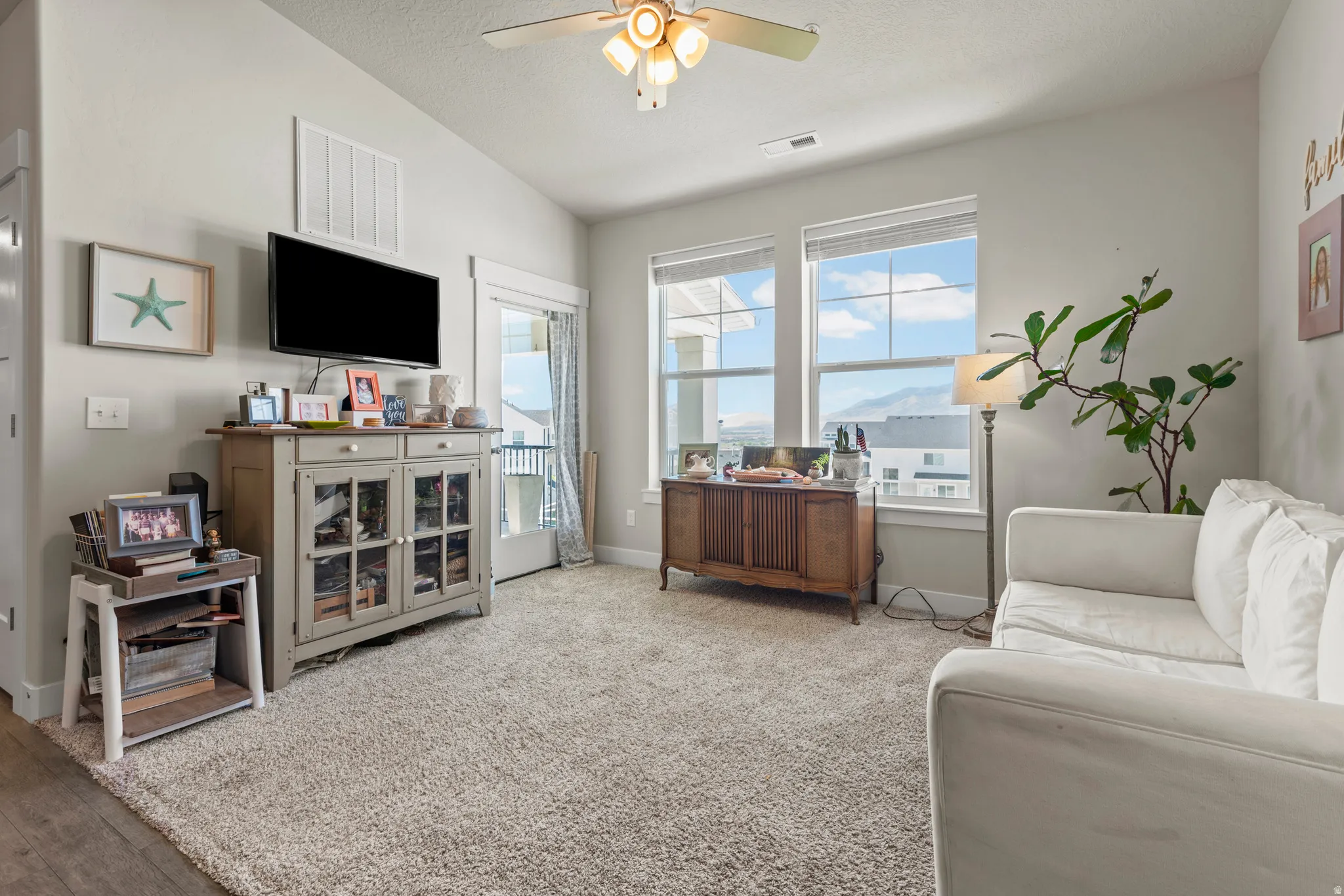 Bright living area featuring a ceiling fan with integrated lighting, a sliding glass door providing outdoor access, and two large windows