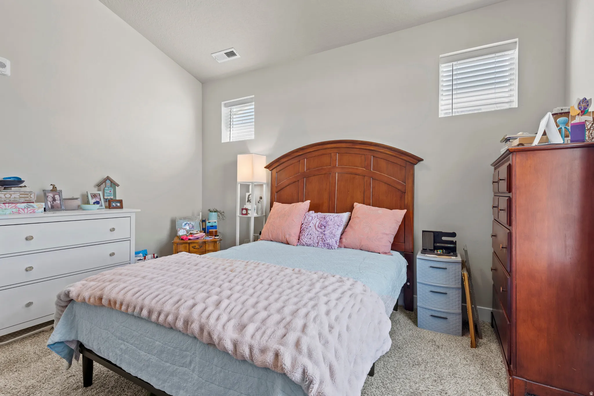 Carpeted room featuring a wooden headboard, light gray walls, and two windows with blinds