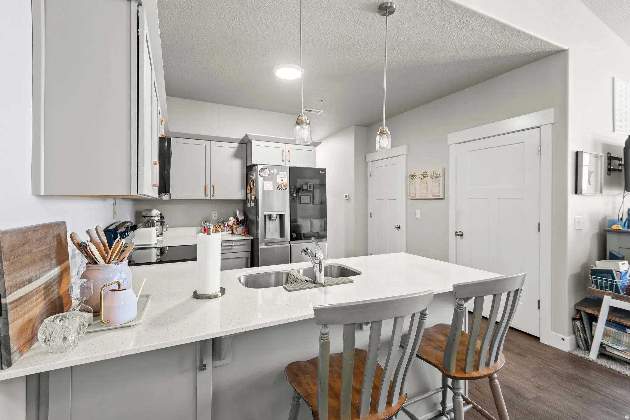 Contemporary kitchen featuring light gray cabinetry, stainless steel appliances, a center island with integrated sink, pendant lighting, and wood-finish flooring