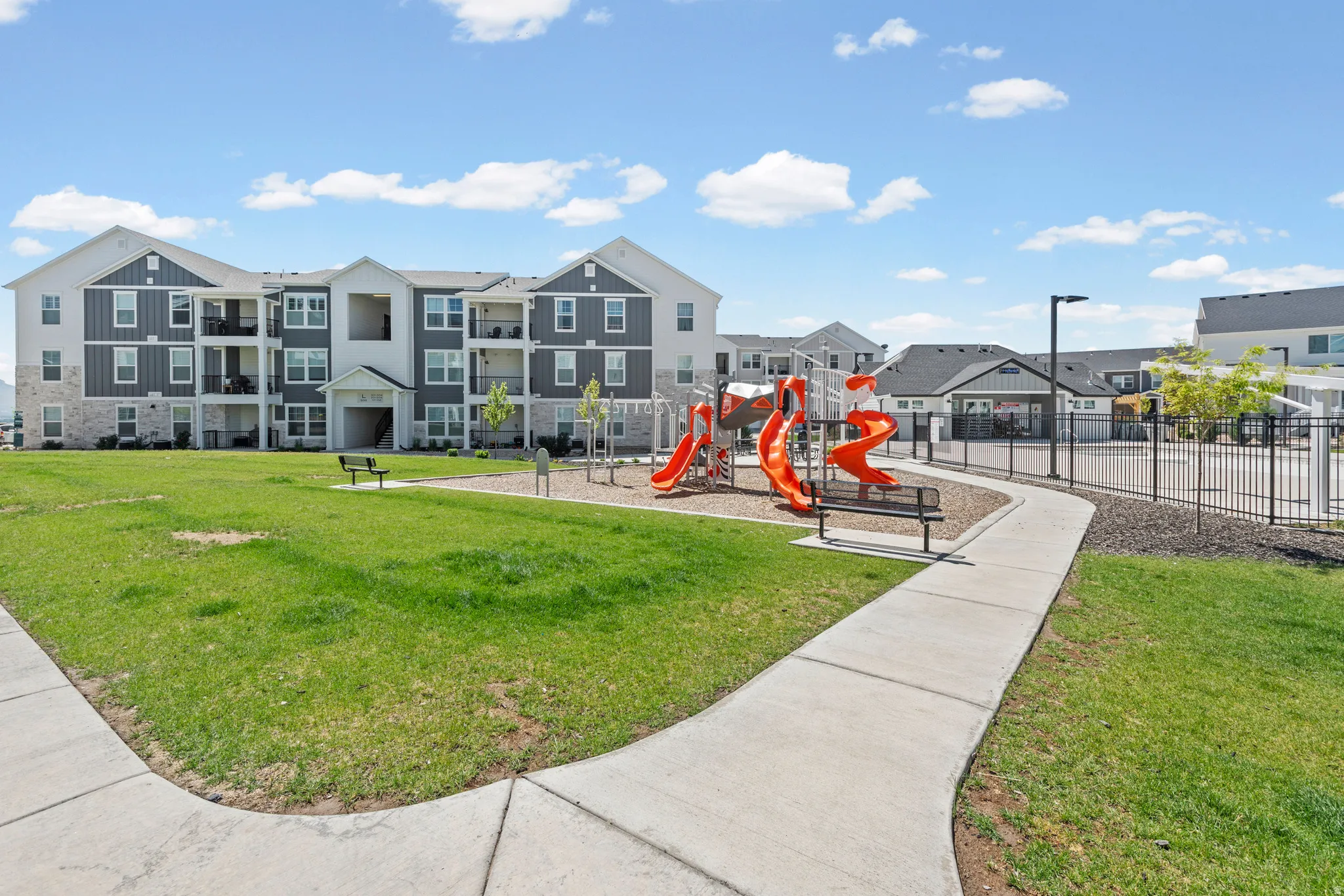 Community green space featuring a playground with slides and swings, a concrete pathway, and a large grassy area