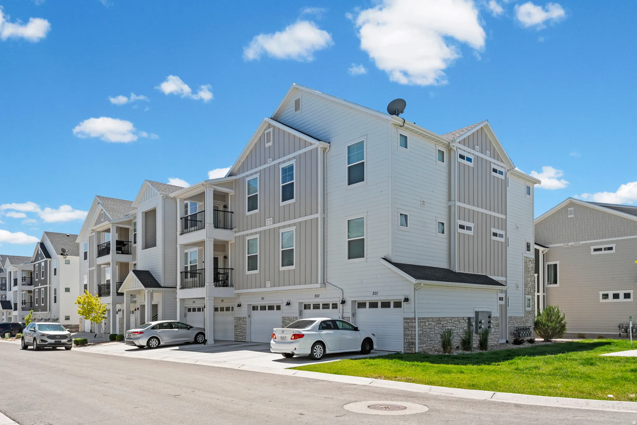 Modern multi-story residential building featuring light-colored siding, dark window frames, and stone accents