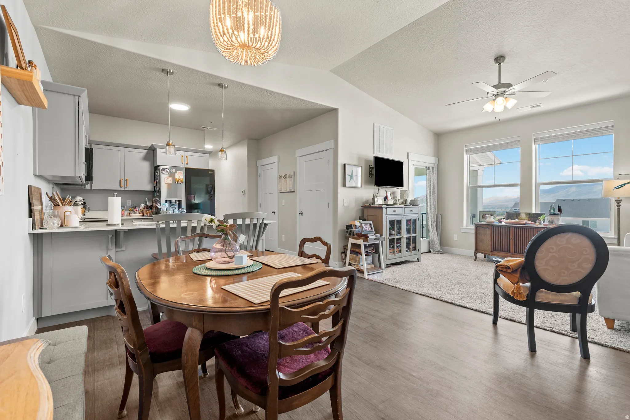 Open-concept living space featuring wood-finish flooring, vaulted ceilings, a contemporary chandelier, and a kitchen with light gray cabinetry and stainless steel appliances