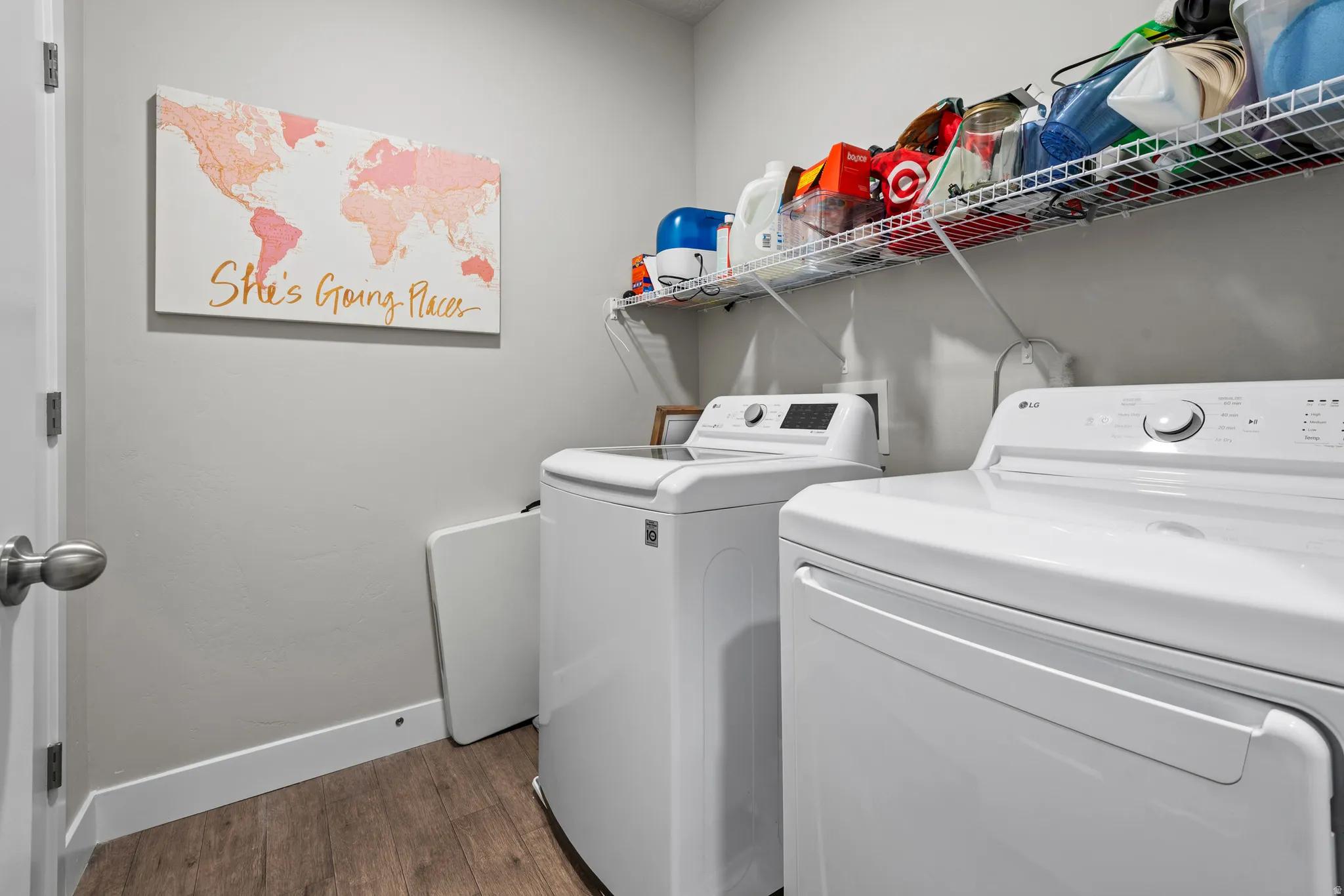 Dedicated laundry area featuring wood-finish flooring, white baseboards, and a wall-mounted wire shelving unit for storage