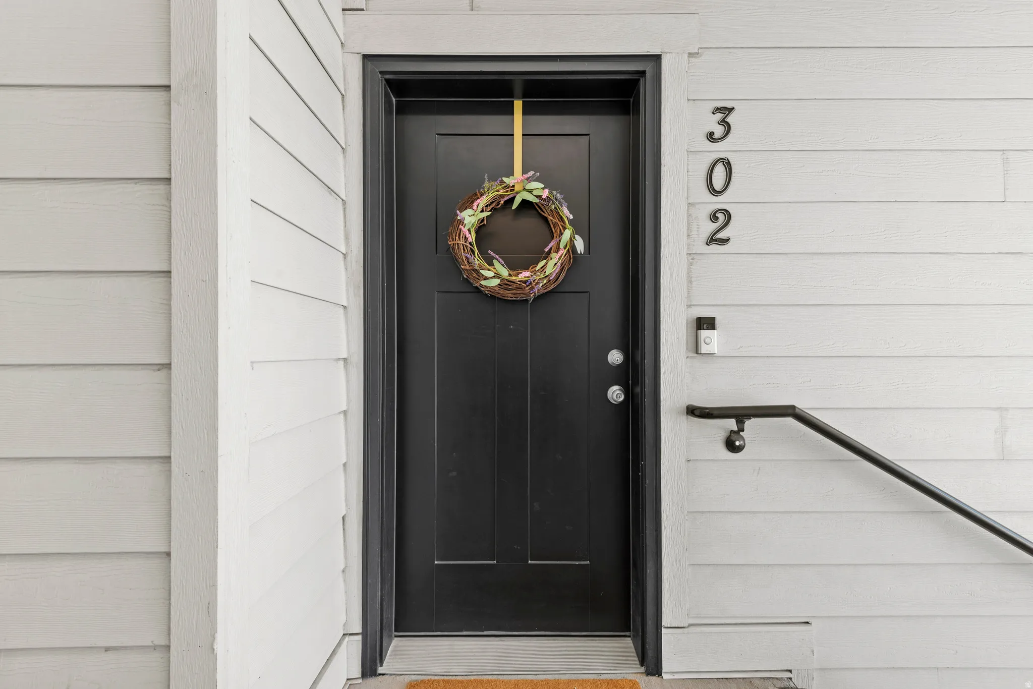 Black paneled entry door with matte black hardware, featuring white horizontal siding