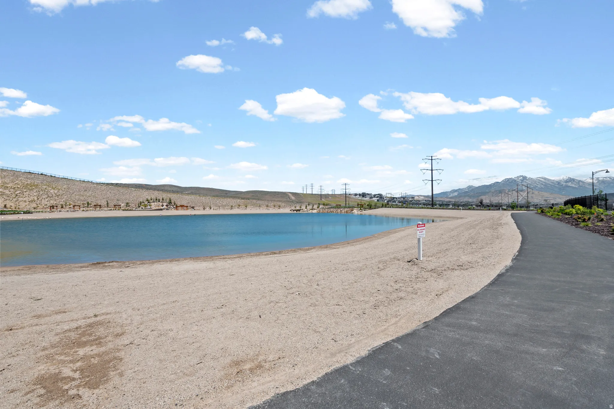 Man-made lake with a sandy shore, bordered by a paved walking path