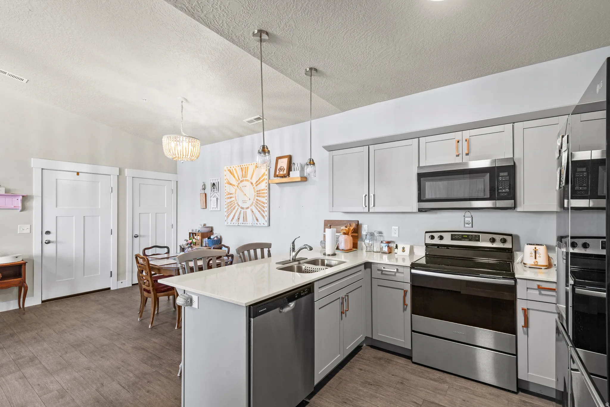 Open-concept kitchen featuring light gray cabinetry, stainless steel appliances, a white countertop island with a built-in sink, and wood-finish flooring
