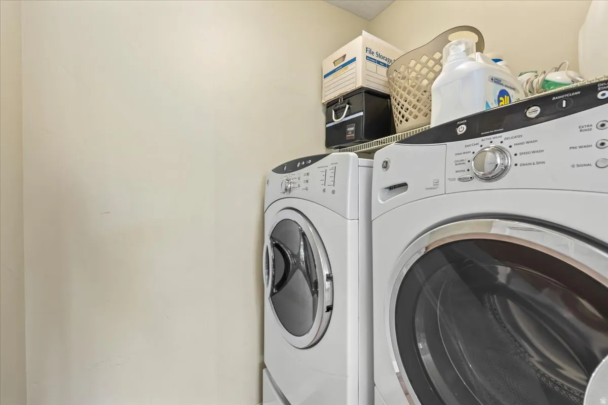 Laundry area featuring a front-loading washer and dryer set, an overhead wire shelf, and light-toned walls