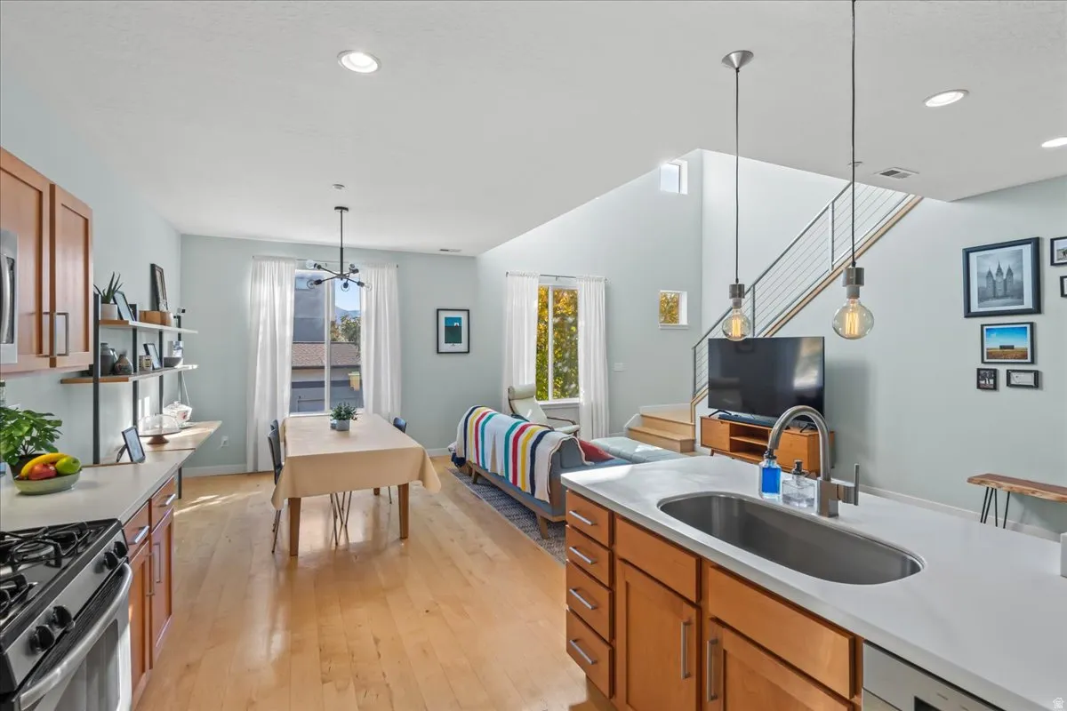 Open-concept living area featuring wood-finish flooring, a kitchen island with an undermount sink and countertop, and a contemporary staircase with cable railing
