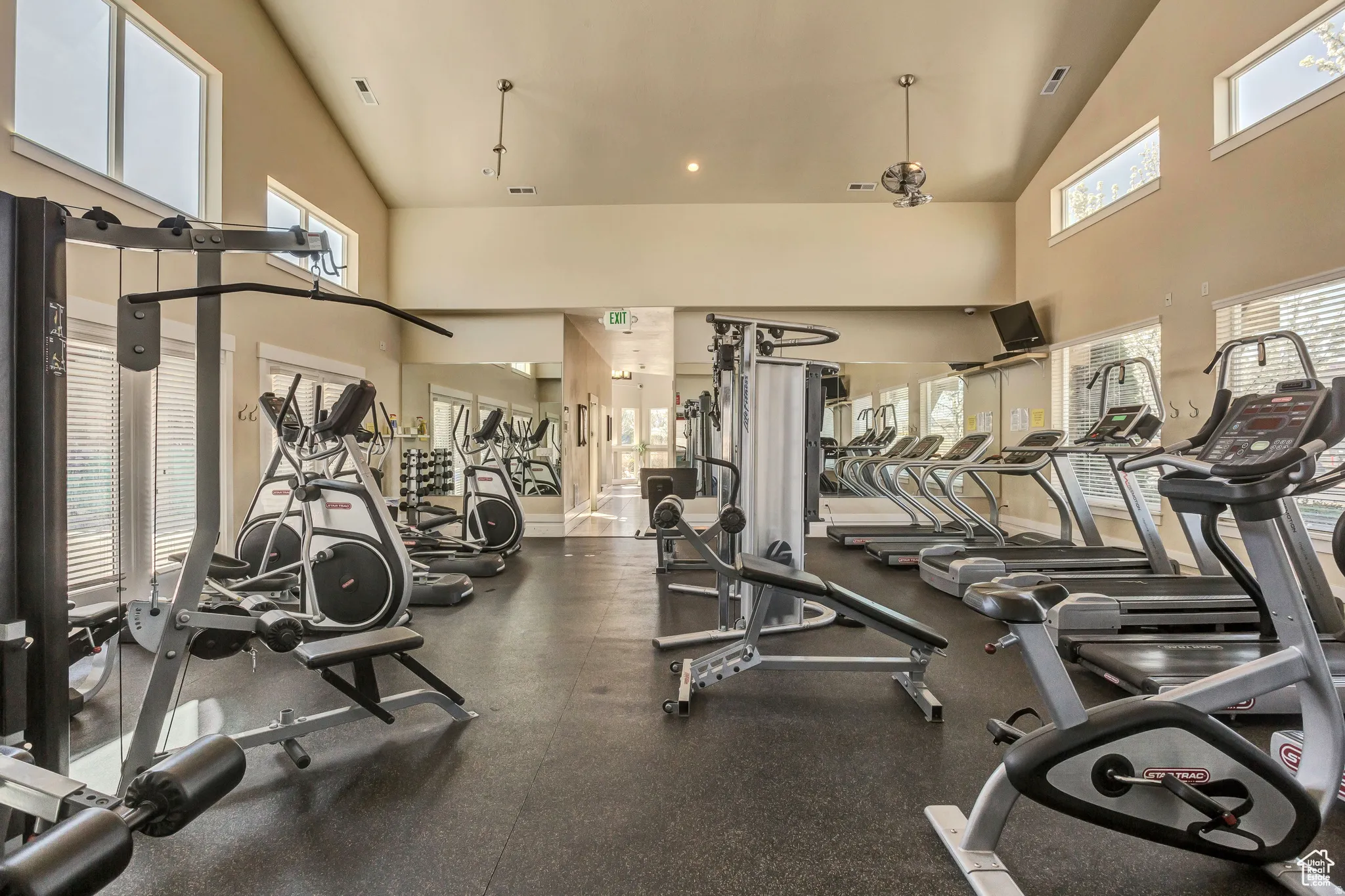 Fitness center featuring a high vaulted ceiling, rubber flooring, mirrored wall, multiple large windows, and various exercise machines