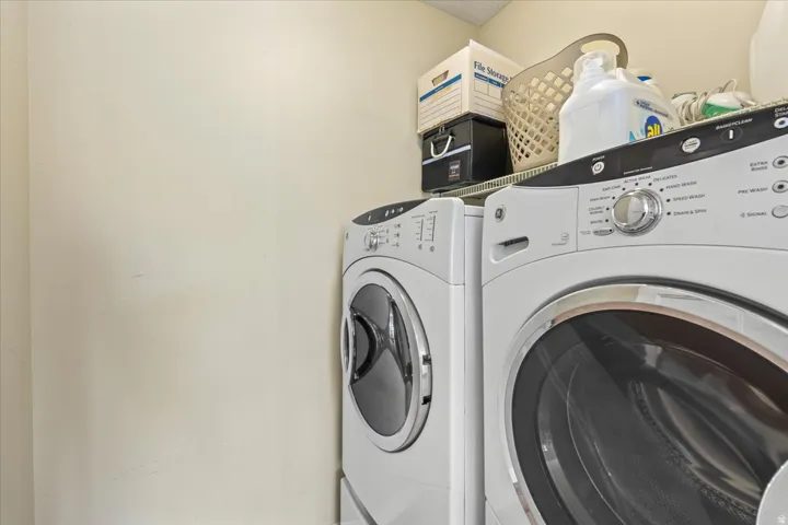 Laundry area featuring a front-loading washer and dryer set, an overhead wire shelf, and light-toned walls