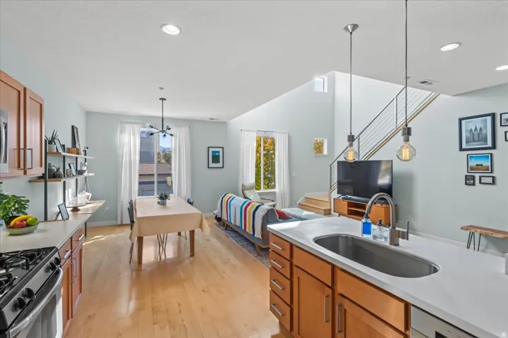 Open-concept living area featuring wood-finish flooring, a kitchen island with an undermount sink and countertop, and a contemporary staircase with cable railing
