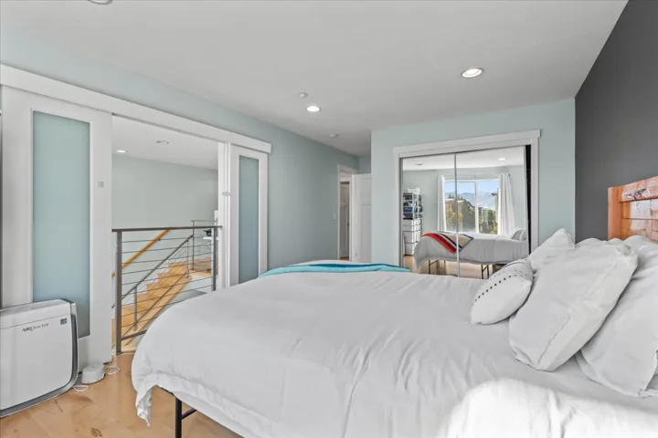 Bedroom featuring light blue walls, wood-finish flooring, recessed lighting, and a mirrored closet