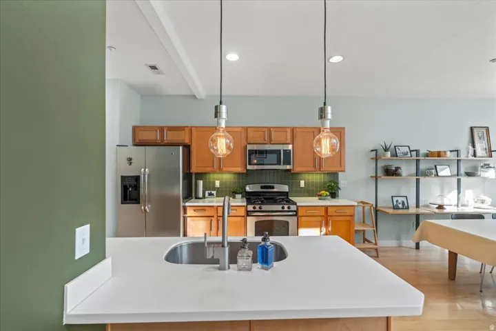 Kitchen featuring a stainless steel French door refrigerator, stainless steel gas range with overhead microwave, natural wood cabinetry, and a white countertop island with an undermount sink