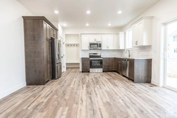 Kitchen featuring wood-finish flooring, stainless steel appliances, light-toned upper cabinetry, dark wood-finish lower cabinetry, and a sliding glass door
