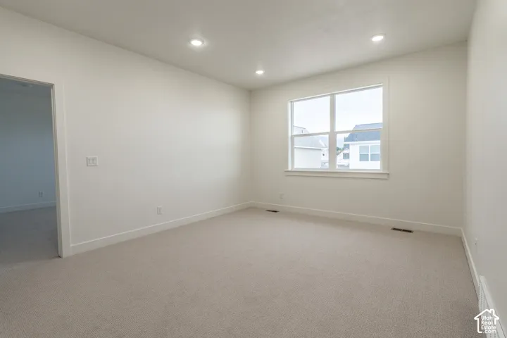 Recessed ceiling lighting illuminates a spacious room featuring neutral-toned carpeting and a large window with white trim