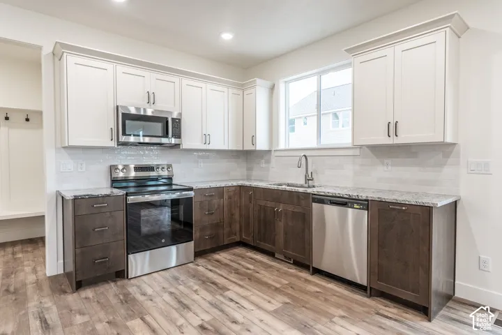 Kitchen featuring wood-finish flooring, two-tone cabinetry, stainless steel appliances, granite countertops, and a subway tile backsplash