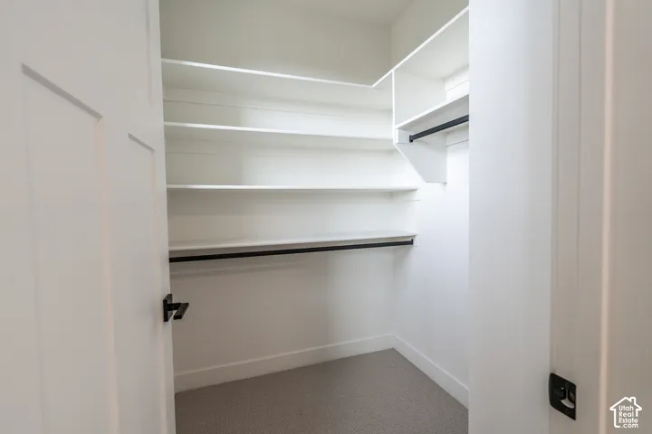 Walk-in closet featuring white built-in shelving, dual clothing rods, and carpeting