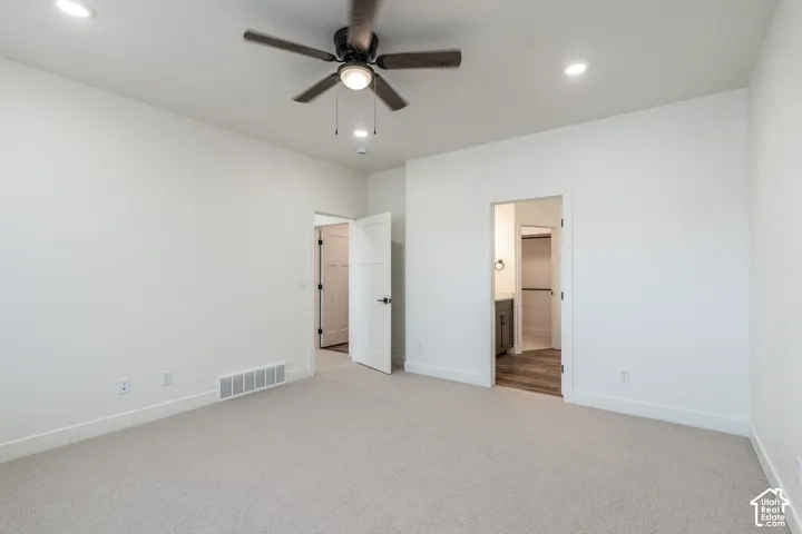 Recessed ceiling lighting, ceiling fan with light fixture, light-toned carpet, white interior doors, and wood-finish flooring visible in the adjoining space