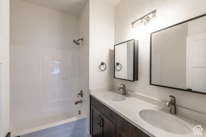 Dual vanity with integrated sinks, brushed nickel fixtures, dark wood-finish cabinetry, and a white shower/tub combination