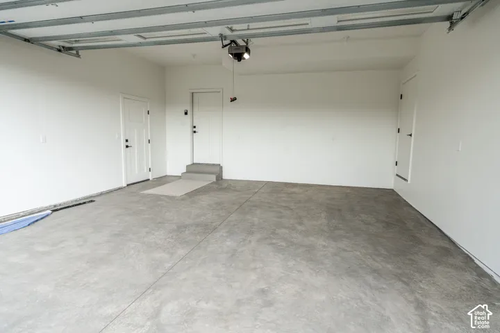 Concrete flooring, white walls, two entry doors, and an automatic garage door opener