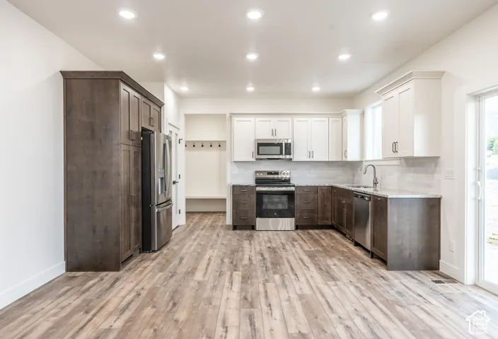 Kitchen featuring stainless steel appliances, wood-finish flooring, recessed lighting, white upper cabinetry, and a subway tile backsplash