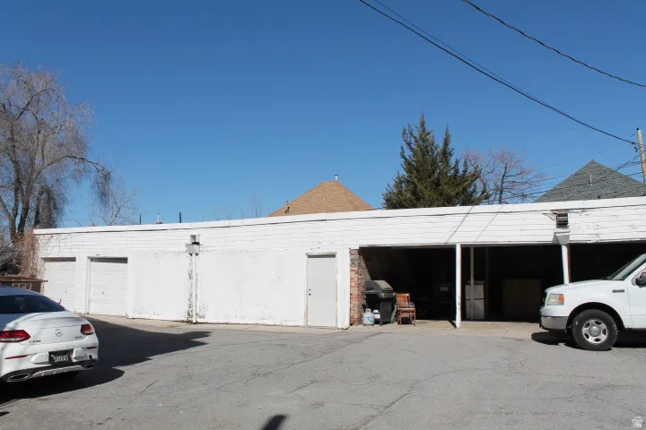 Detached garage structure featuring multiple bays, a covered carport area, white siding, and a paved lot