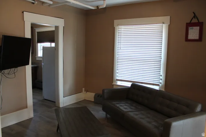 Living area featuring wood-finish flooring, a window with blinds, and white trim