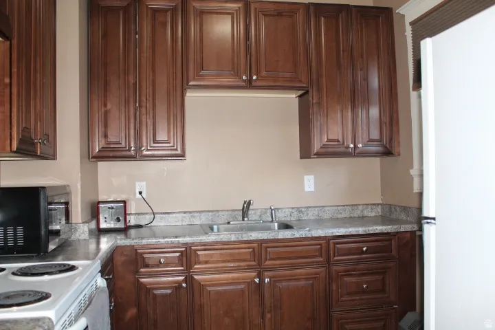 Kitchen featuring wood-finish cabinetry, a double basin stainless steel sink, and speckled countertops
