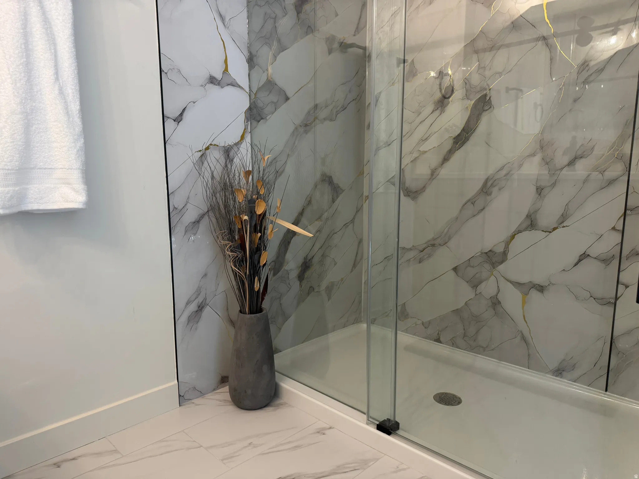 Glass-enclosed shower featuring large format tile with white and grey veining and gold accents