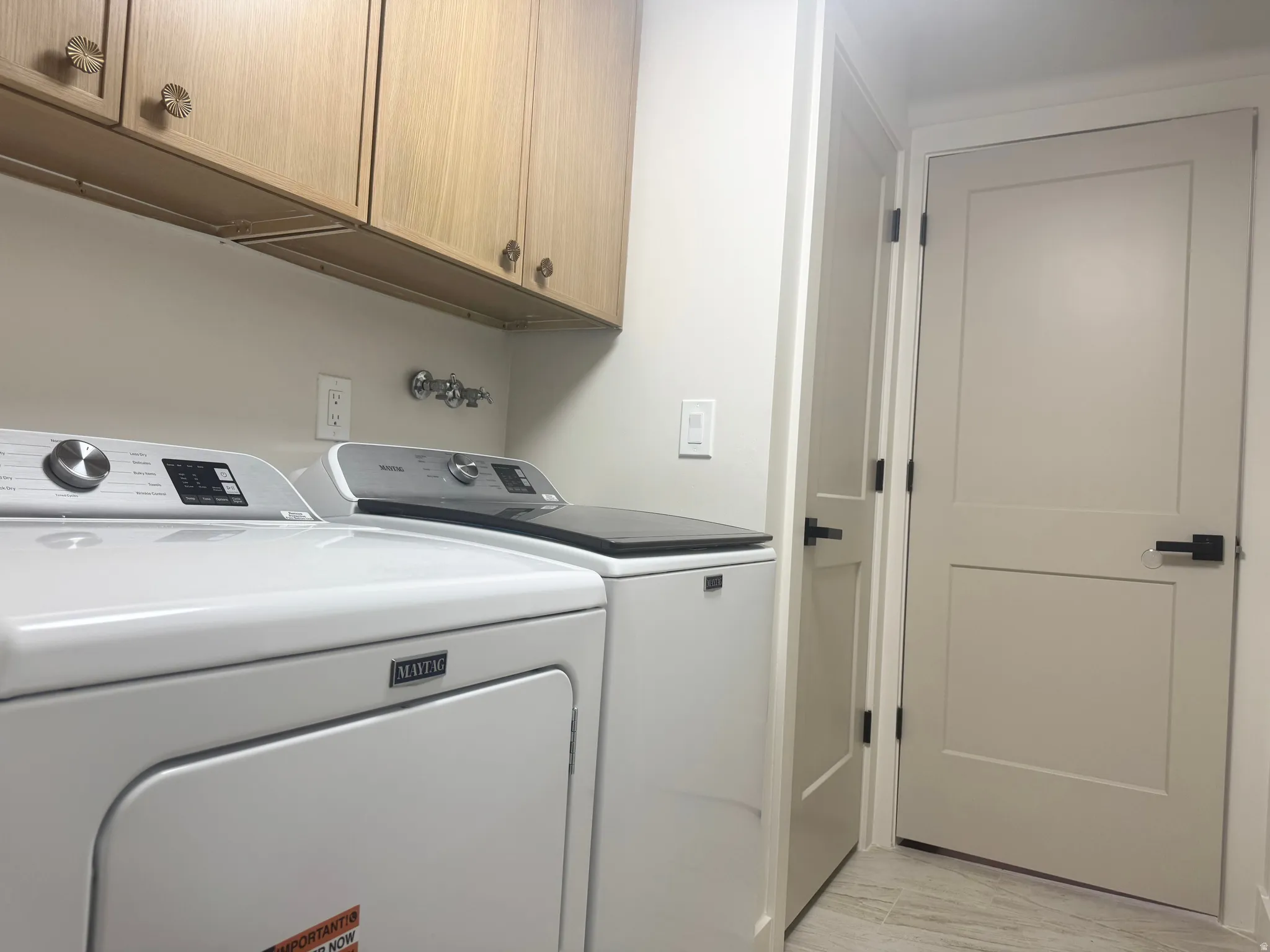 Dedicated laundry space featuring light wood-finish cabinetry with decorative hardware, a wall-mounted utility faucet, and neutral wall paint