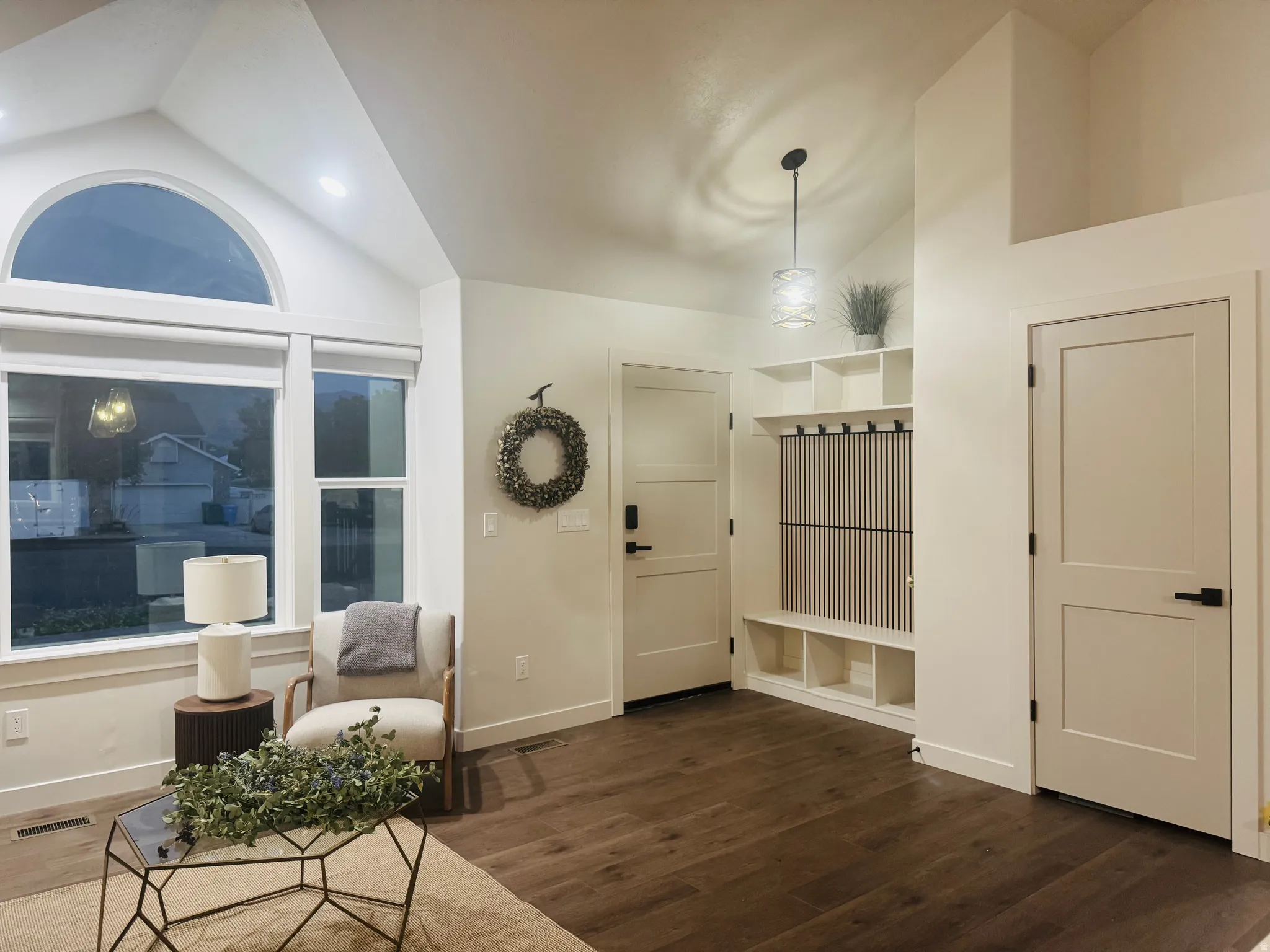 Vaulted ceiling with an arched transom window, wood-finish flooring, built-in shelving, a modern pendant light fixture, and white interior doors with black hardware