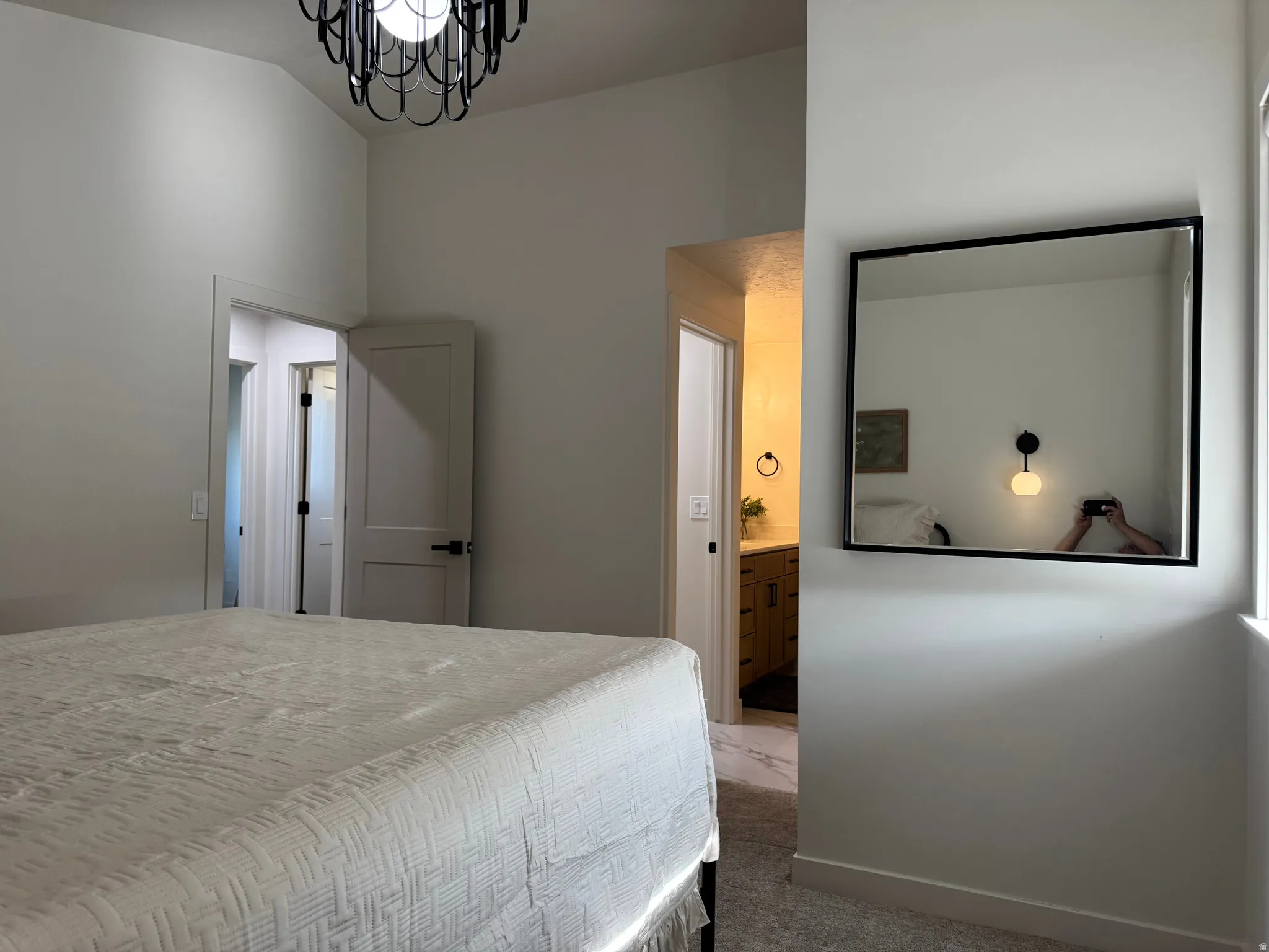 Bedroom featuring vaulted ceilings, a contemporary black chandelier, neutral wall tones, and carpet flooring