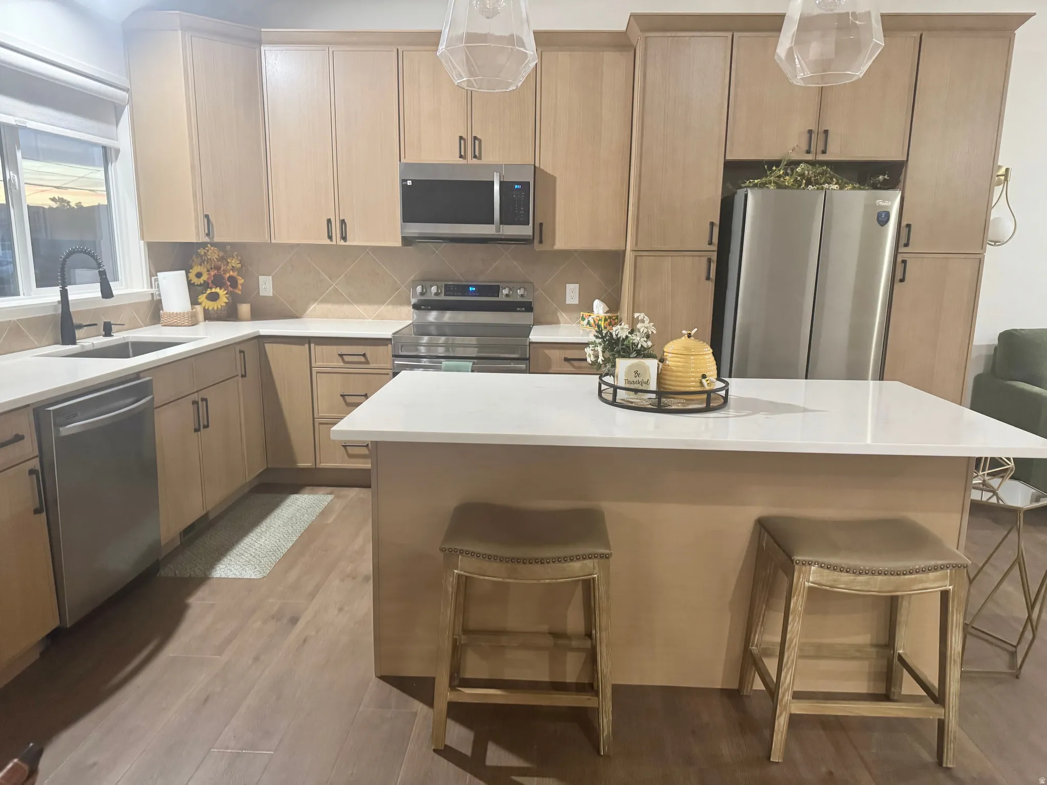 Contemporary kitchen featuring light wood-finish cabinetry, stainless steel appliances, a center island with a white countertop, and wood-finish flooring