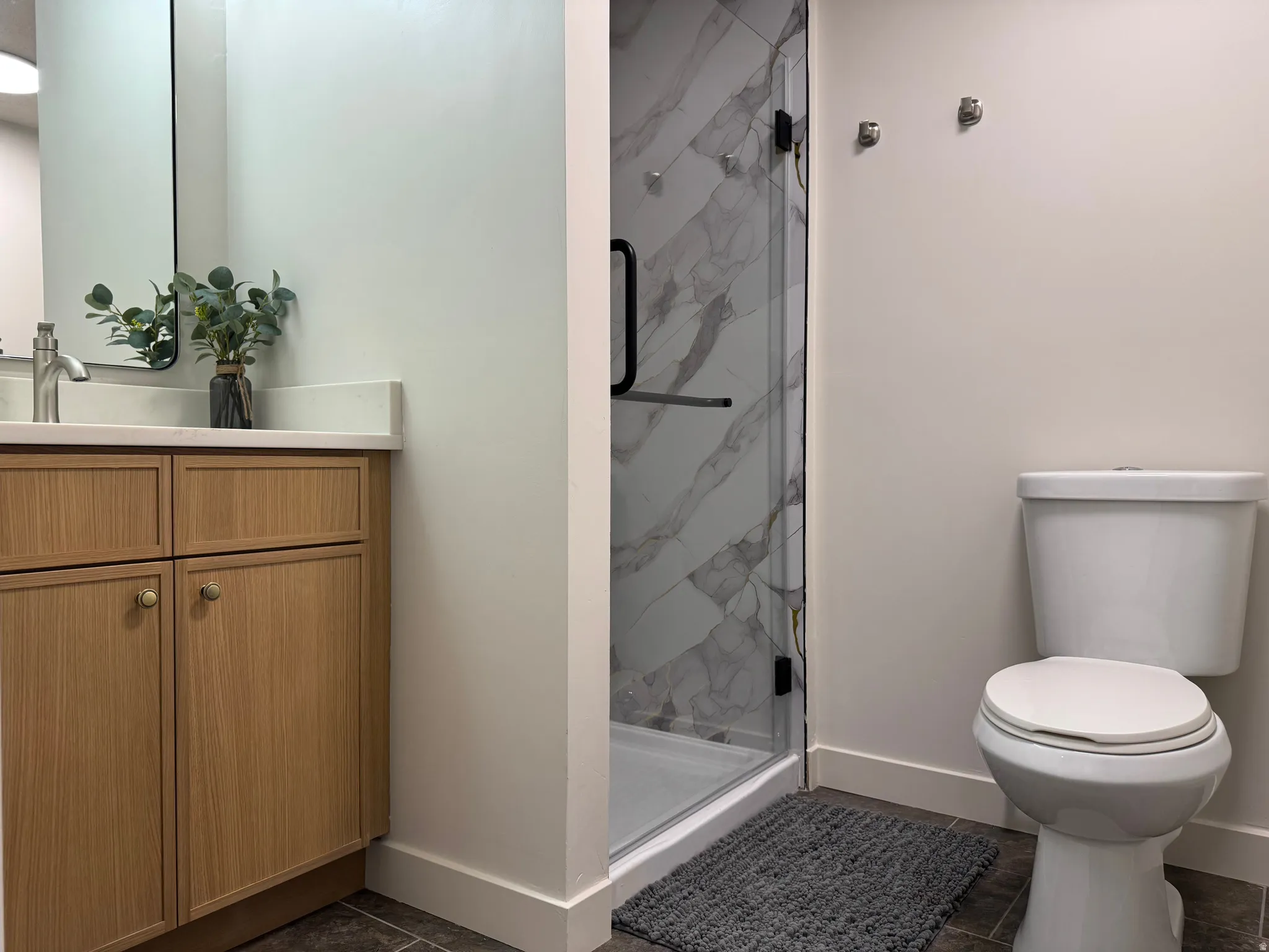 Bathroom featuring a glass-enclosed shower with large format marble-look tile, a wood-finish vanity with a light-colored countertop, and a contemporary toilet