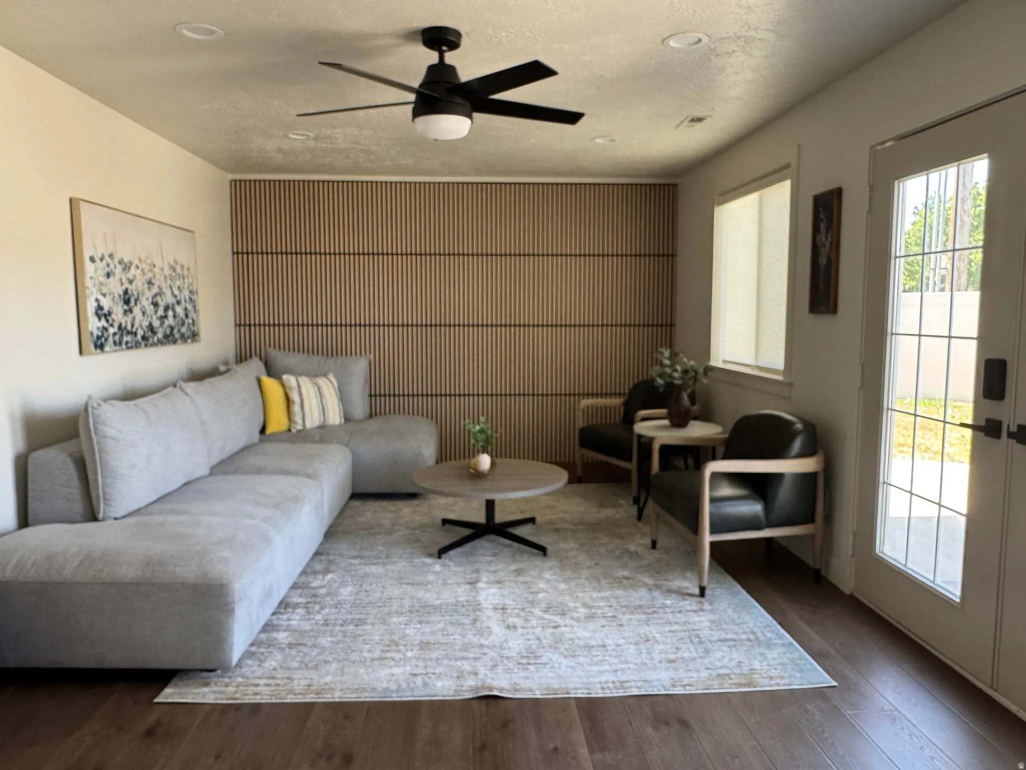 Living area featuring wood-finish flooring, a contemporary ceiling fan with integrated lighting, recessed ceiling lights, a paneled accent wall, and a glass-paned exterior door
