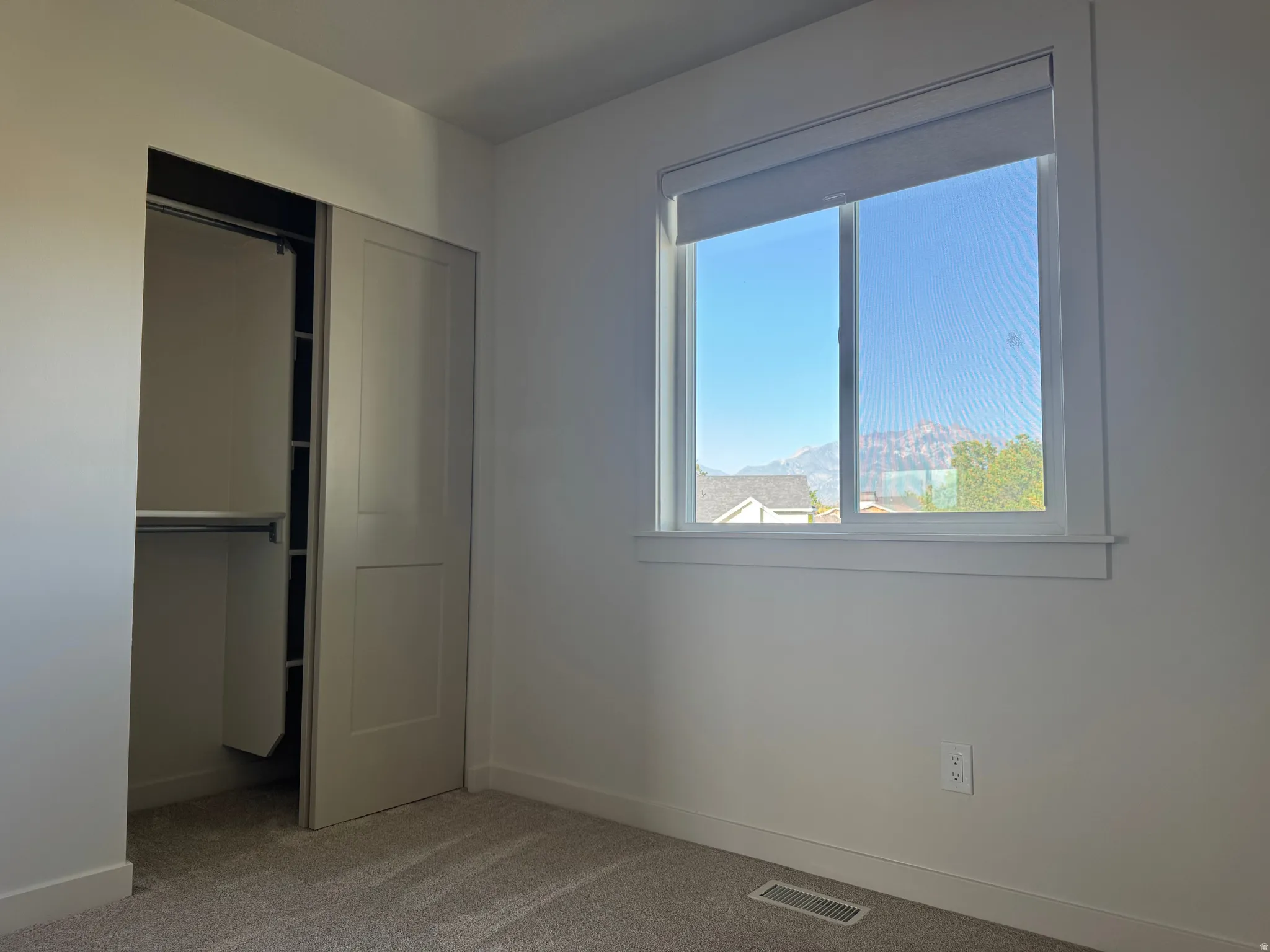 Bedroom featuring carpet flooring, a window with roller shades, and a closet with sliding panel doors and built-in shelving