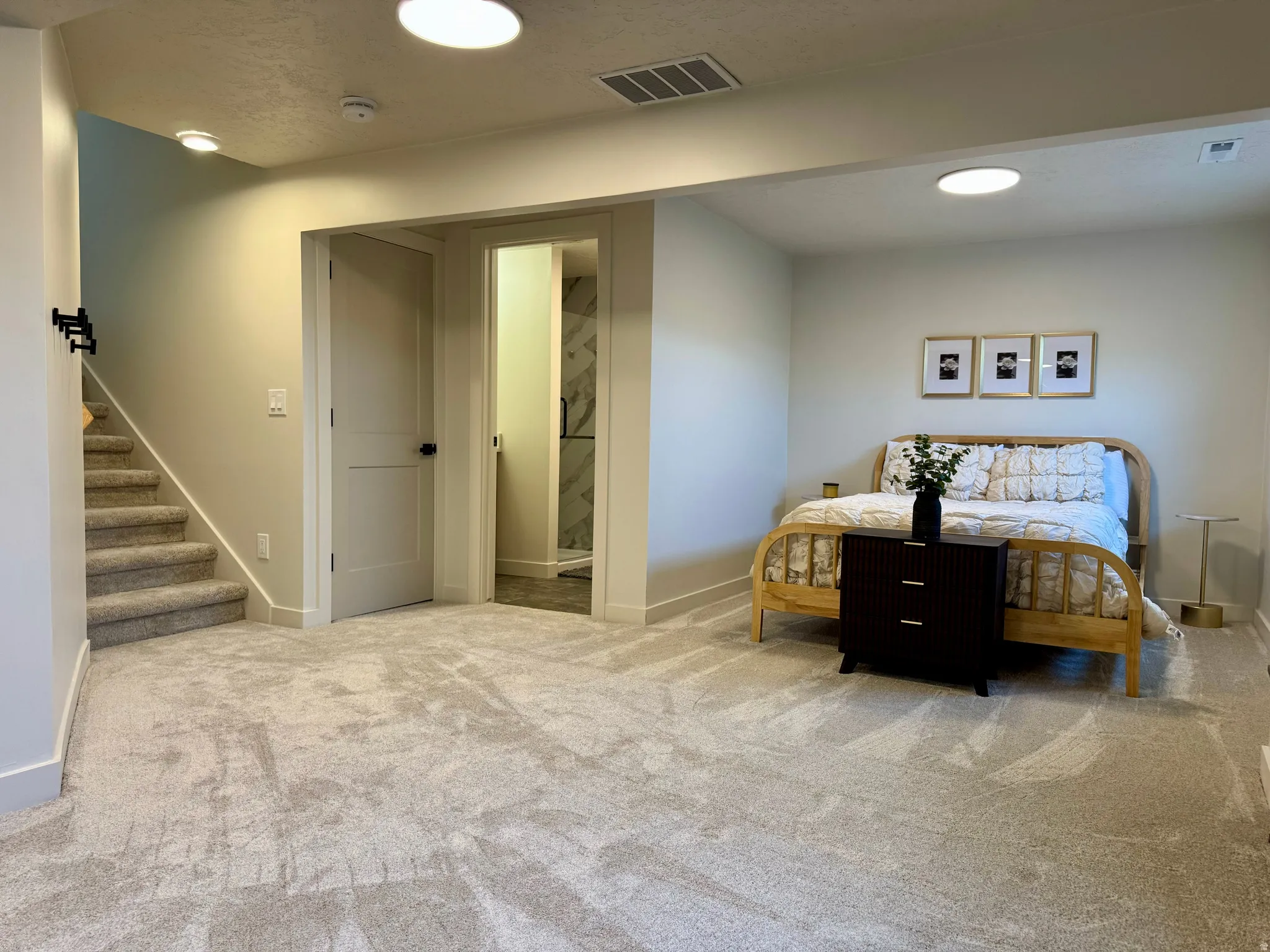 Expansive carpeted room featuring a staircase with carpeted treads, a solid door with black hardware, and an additional doorway revealing a bathroom with a glass shower enclosure and tiled walls