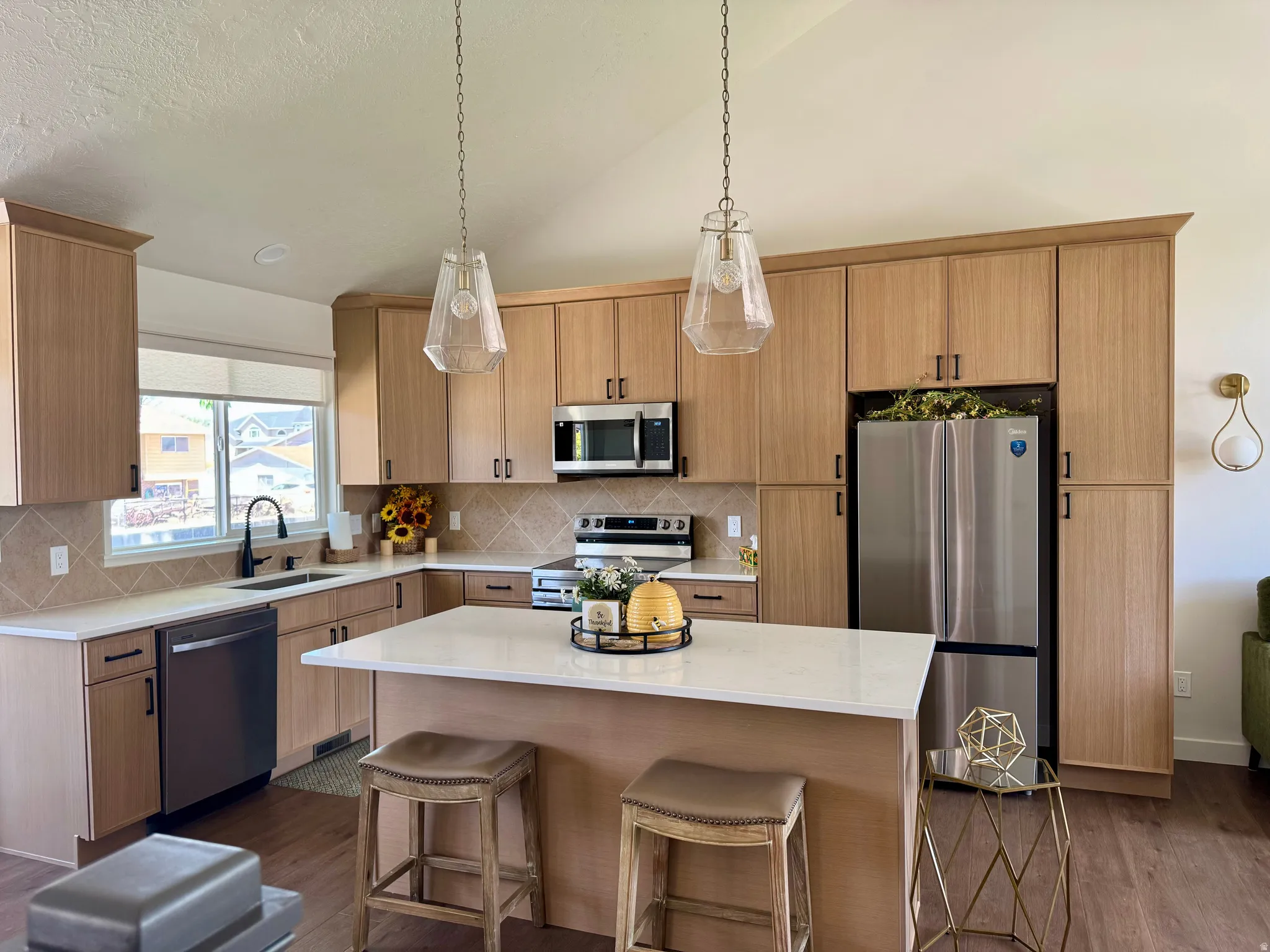 Modern kitchen featuring wood-finish cabinetry, stainless steel appliances, a center island with countertop seating, and two pendant light fixtures