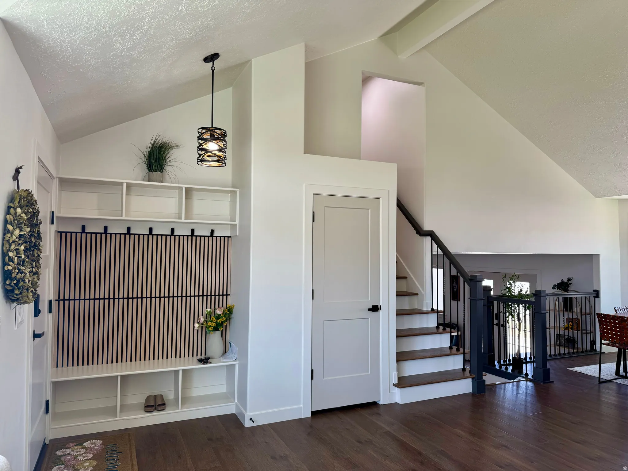 Vaulted ceiling entryway featuring a built-in hall tree with storage, wood-finish flooring, and a modern stair railing